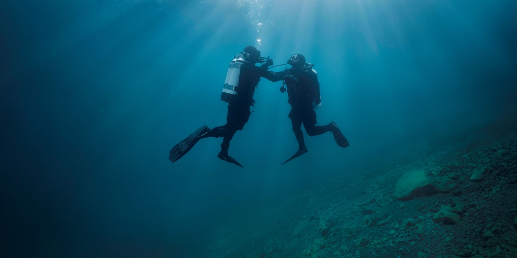 Scène sous-marine : un plongeur soutient un autre plongeur qui a des problèmes d'alimentation en oxygène.